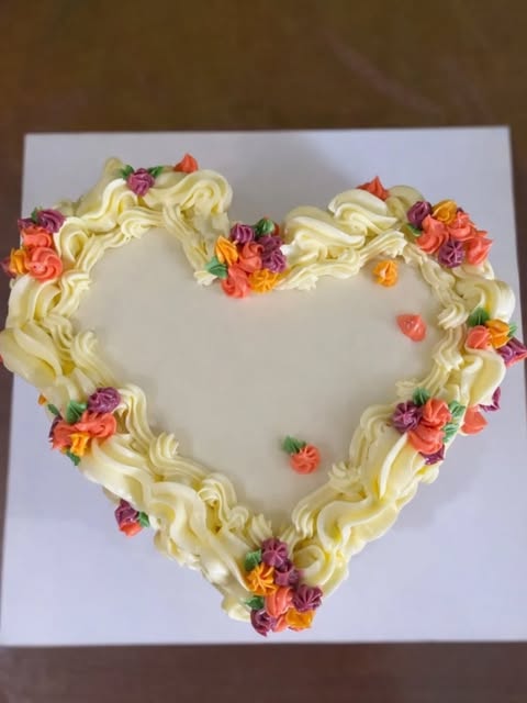 Torta con forma de corazón decorada con buttercream y florcitas de colores